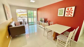 Uma sala de estar moderna com um sofá, uma mesa de jantar, cadeiras, uma televisão e obras de arte na parede.