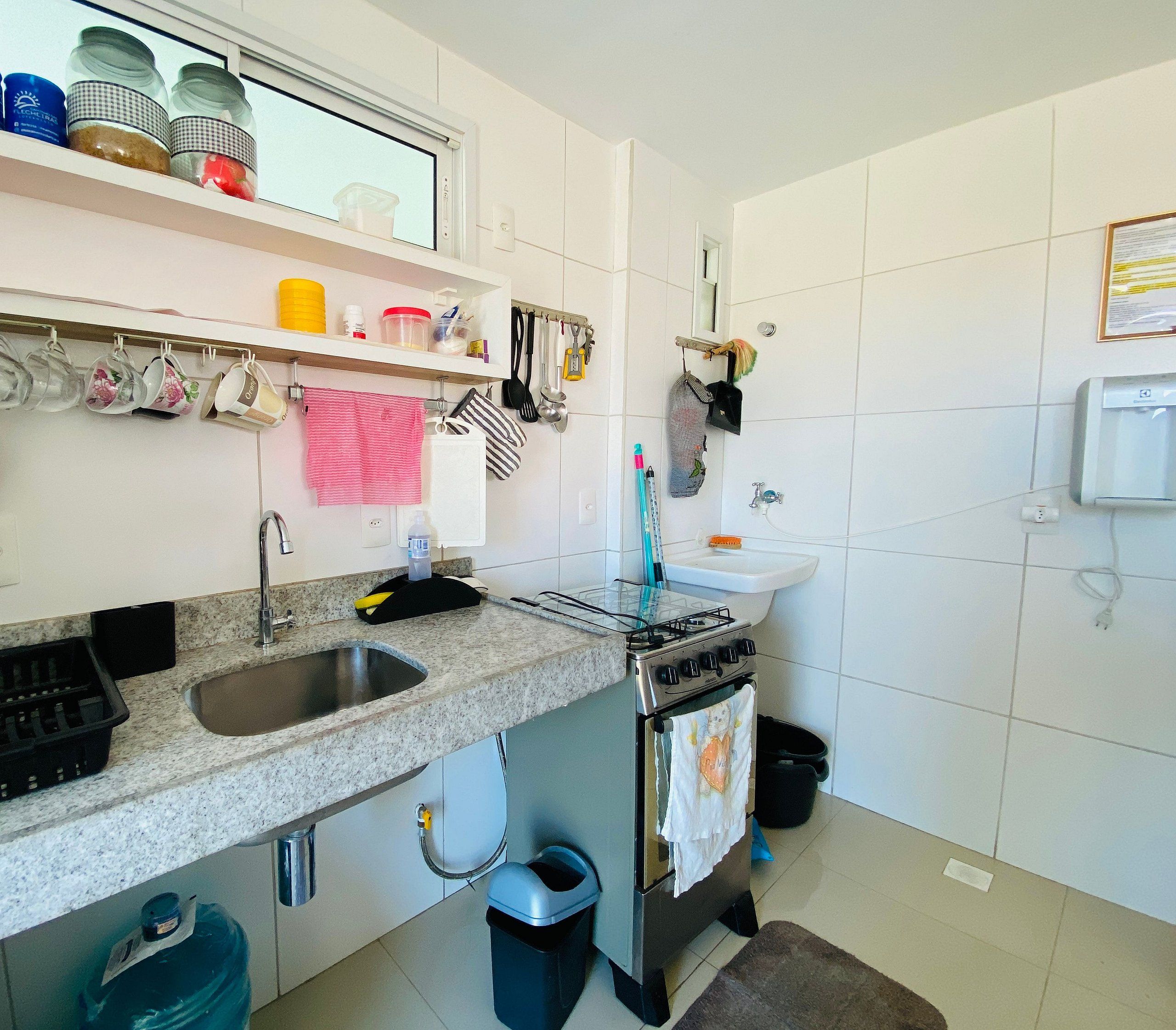 A kitchen with a granite countertop, stainless steel sink, and a gas stove. There are hanging utensils and a trash bin.