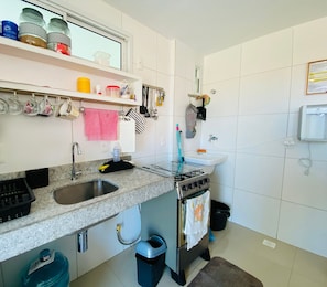 A kitchen with a granite countertop, stainless steel sink, and a gas stove. There are hanging utensils and a trash bin. - Solarium Residence Resort (Aquiraz)