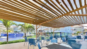 An outdoor seating area with tables and chairs, a pool, and a covered walkway. - Solarium Residence Resort (Aquiraz)