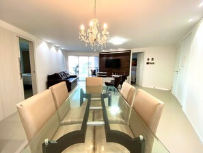 Una sala de estar moderna con una mesa de comedor de vidrio, sofás de cuero, una araña y un televisor montado en la pared.