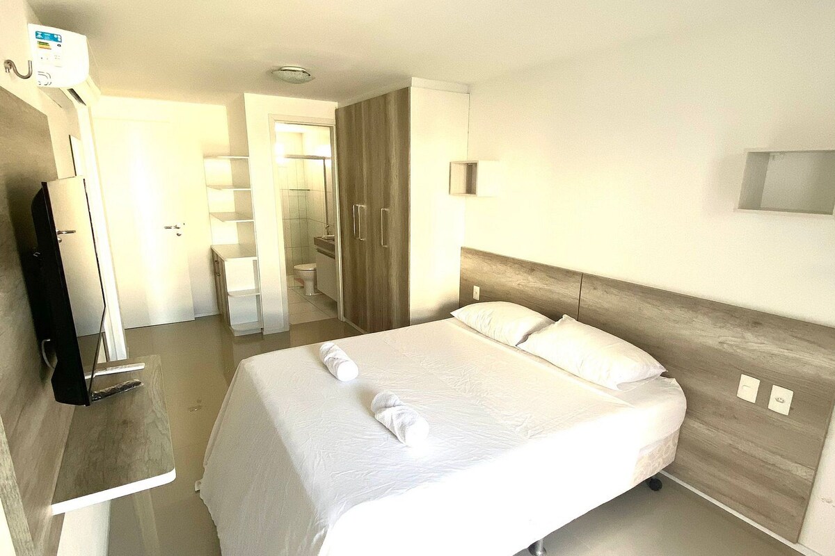 Una habitación de hotel moderna con una cama grande, mesitas de noche, un televisor de pantalla plana y un baño visible a través de una puerta abierta.