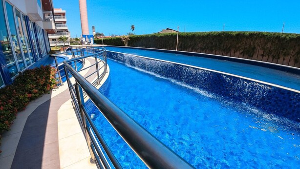 Una piscina con diseño curvo, rodeada por un edificio con balcones y cielo despejado.