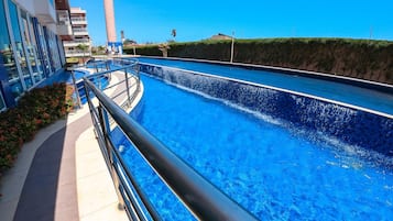 Piscina com design curvo, cercada por um edifício com varandas e céu claro.