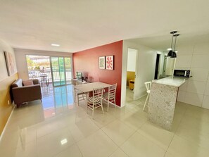 Amplia sala de estar con mesa de comedor, sillas, sofá y una zona de cocina con microondas.