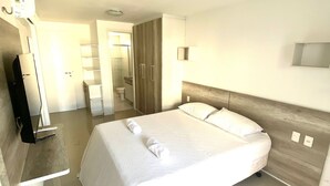 Una habitación de hotel moderna con una cama grande, mesitas de noche, un televisor de pantalla plana y un baño visible a través de una puerta abierta.