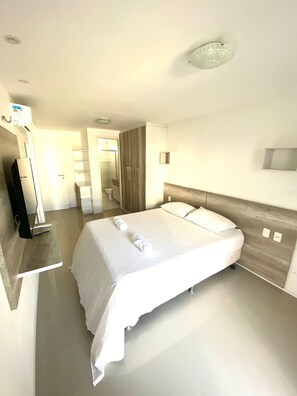 Quarto de hotel moderno com uma cama grande, mesas de cabeceira, televisão de tela plana e um banheiro visível através de uma porta aberta.