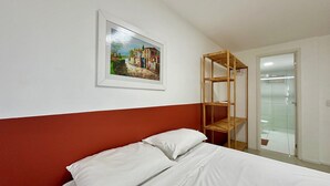 A bedroom with a bed, a framed painting, and a wooden shelf unit. - Solarium Residence Resort (Aquiraz)