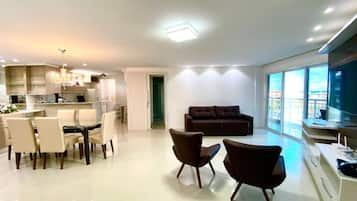 Una sala de estar moderna con un sofá, sillas, un televisor y un comedor con una mesa y sillas.