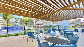 Área de pátio externa com mesas, cadeiras, piscina e vista para edifícios ao redor.