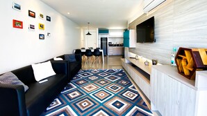 A modern living room with a black sofa, a patterned rug, and a kitchen in the background. - Solarium Residence Resort (Aquiraz)