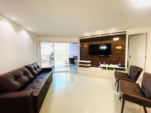 A modern living room with a sofa, chairs, a TV, and a balcony.