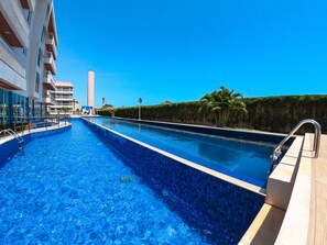 Una piscina con un cielo azul despejado, un rascacielos al fondo y una palmera.