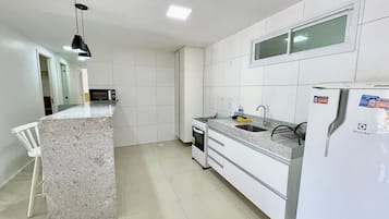 A kitchen with white cabinets, a granite countertop, a microwave, a stove, a sink, and a refrigerator.