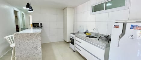Cocina con armarios blancos, encimera de granito, microondas, estufa, fregadero y refrigerador.