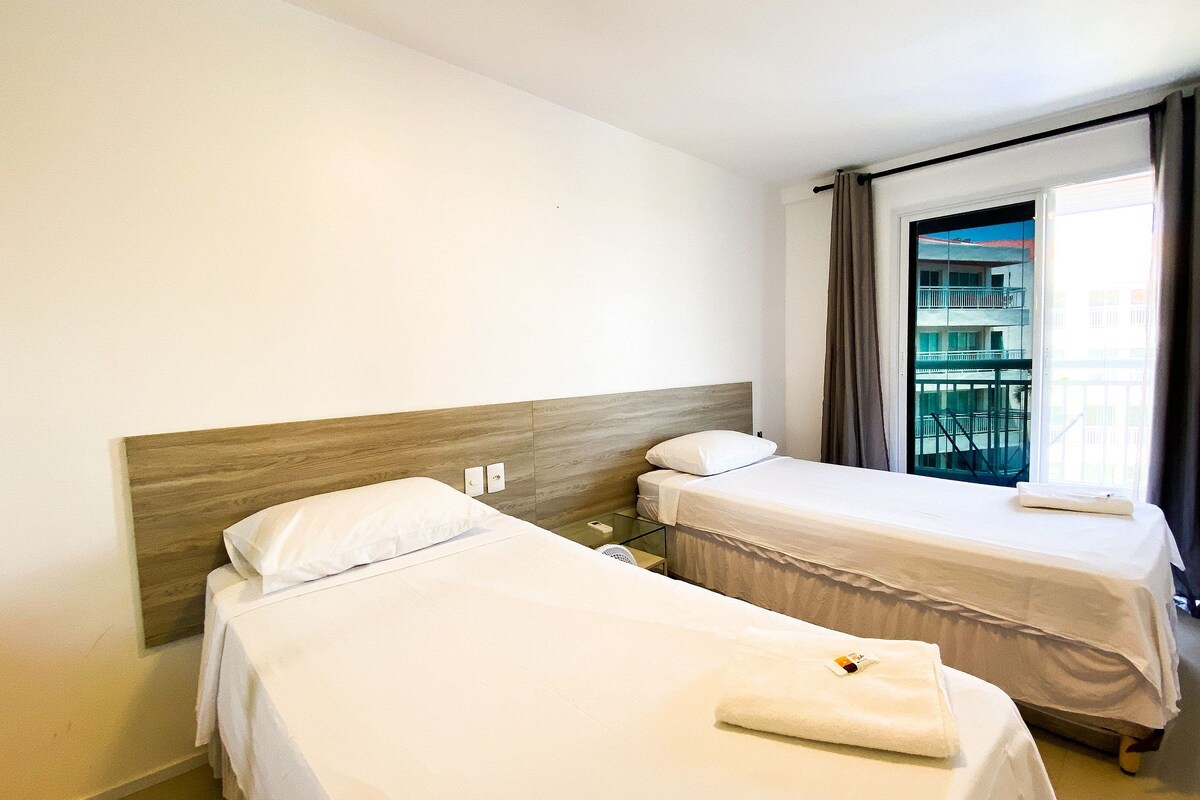 Habitación de hotel con dos camas individuales, cabecera de madera, ventana con vistas a un edificio y balcón.