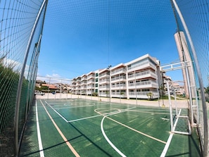 A basketball court with a netted enclosure, surrounded by a multi-story building with balconies.