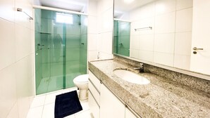 Un baño con cabina de ducha de vidrio, un inodoro blanco, un lavamanos con encimera de granito y un espejo grande.