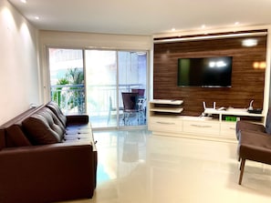 A modern living room with a sofa, TV, and a balcony with outdoor furniture. - Solarium Residence Resort (Aquiraz)