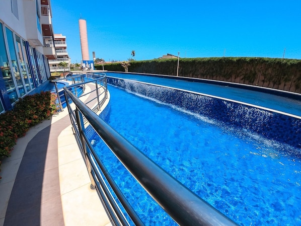 Una piscina con diseño curvo, rodeada por un edificio con balcones y cielo despejado.