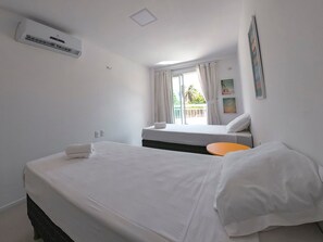 Quarto de hotel com cama, uma pequena mesa, janela com cortinas e um ar condicionado.