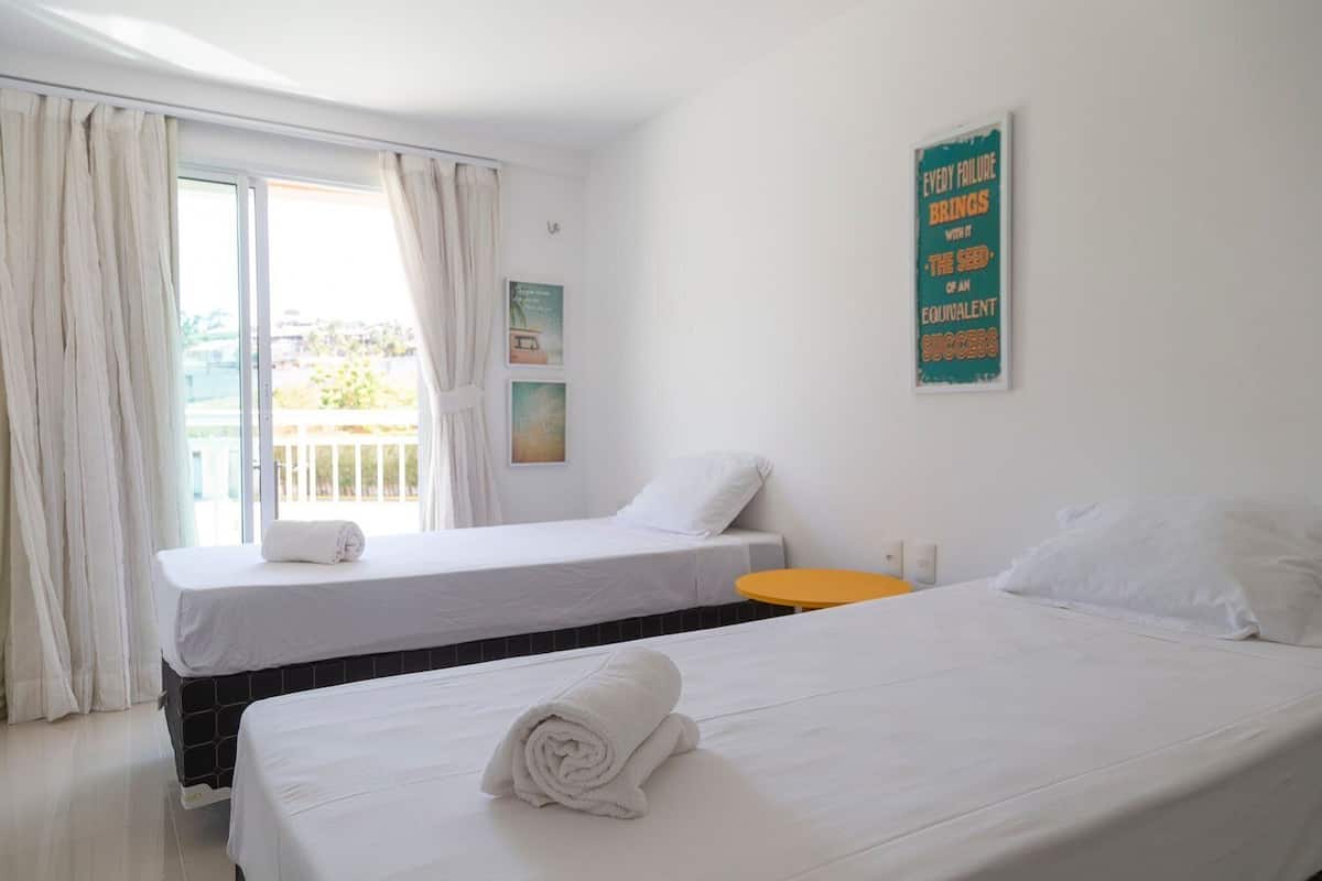 A hotel room with two beds, a small orange table, and a balcony with curtains.