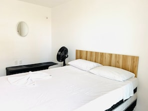 Habitación de hotel con una cama, un espejo redondo, un ventilador negro y un cabecero de madera.