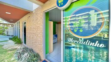A Mercadinho hotel entrance with a 24-hour home market sign, a blue mat, and a green door.
