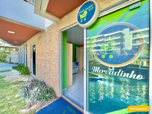 Entrada del hotel Mercadinho con un letrero de mercado de día completo, una alfombra azul y una puerta verde.