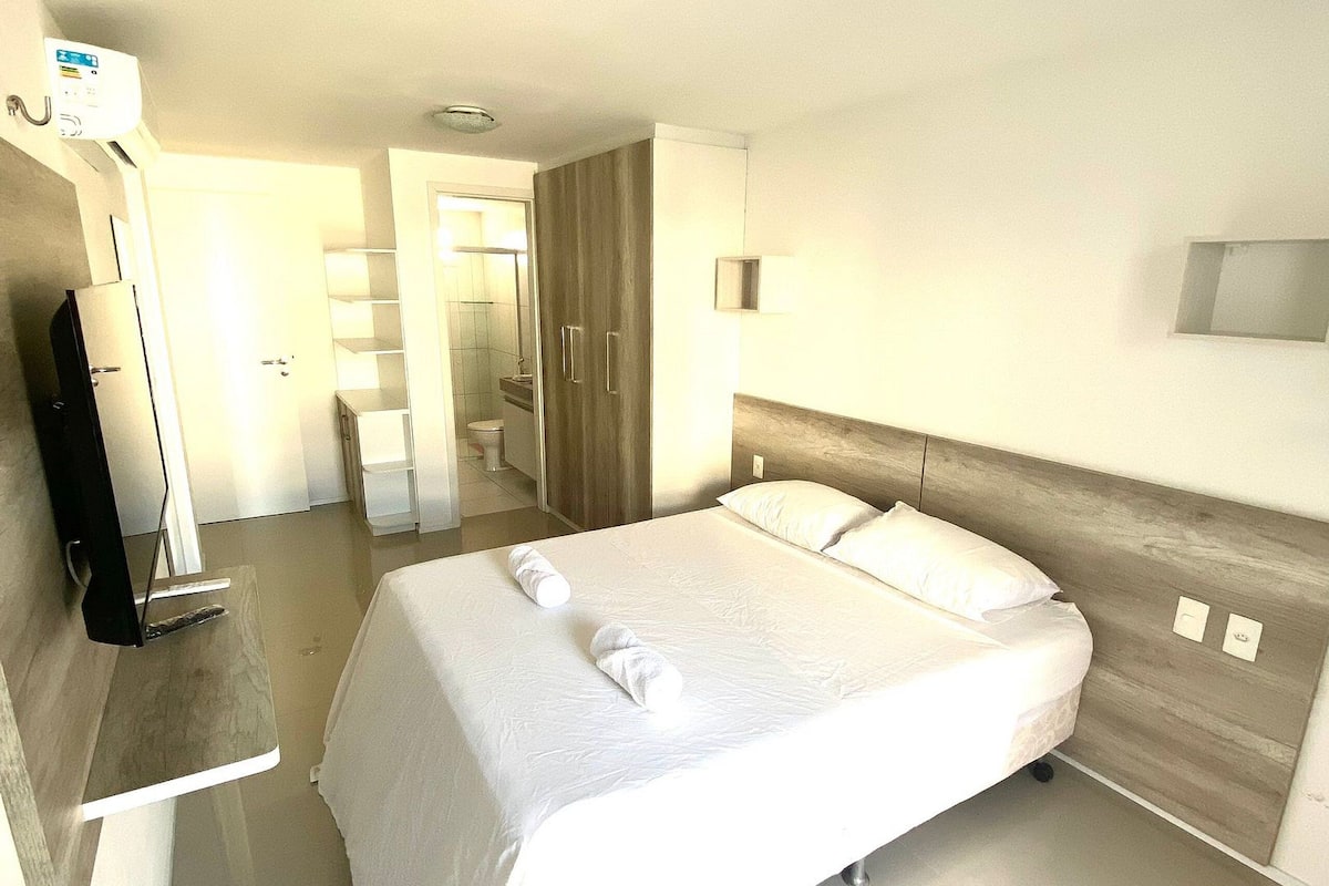 A modern hotel room with a large bed, bedside tables, a flat-screen TV, and a bathroom visible through an open door.