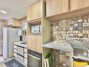 Una cocina con armarios de madera, microondas integrado, horno de acero inoxidable y salpicadero con azulejos de estilo vintage.