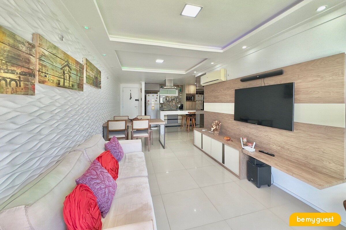 Una sala de estar moderna con un sofá, un televisor y una cocina al fondo.
