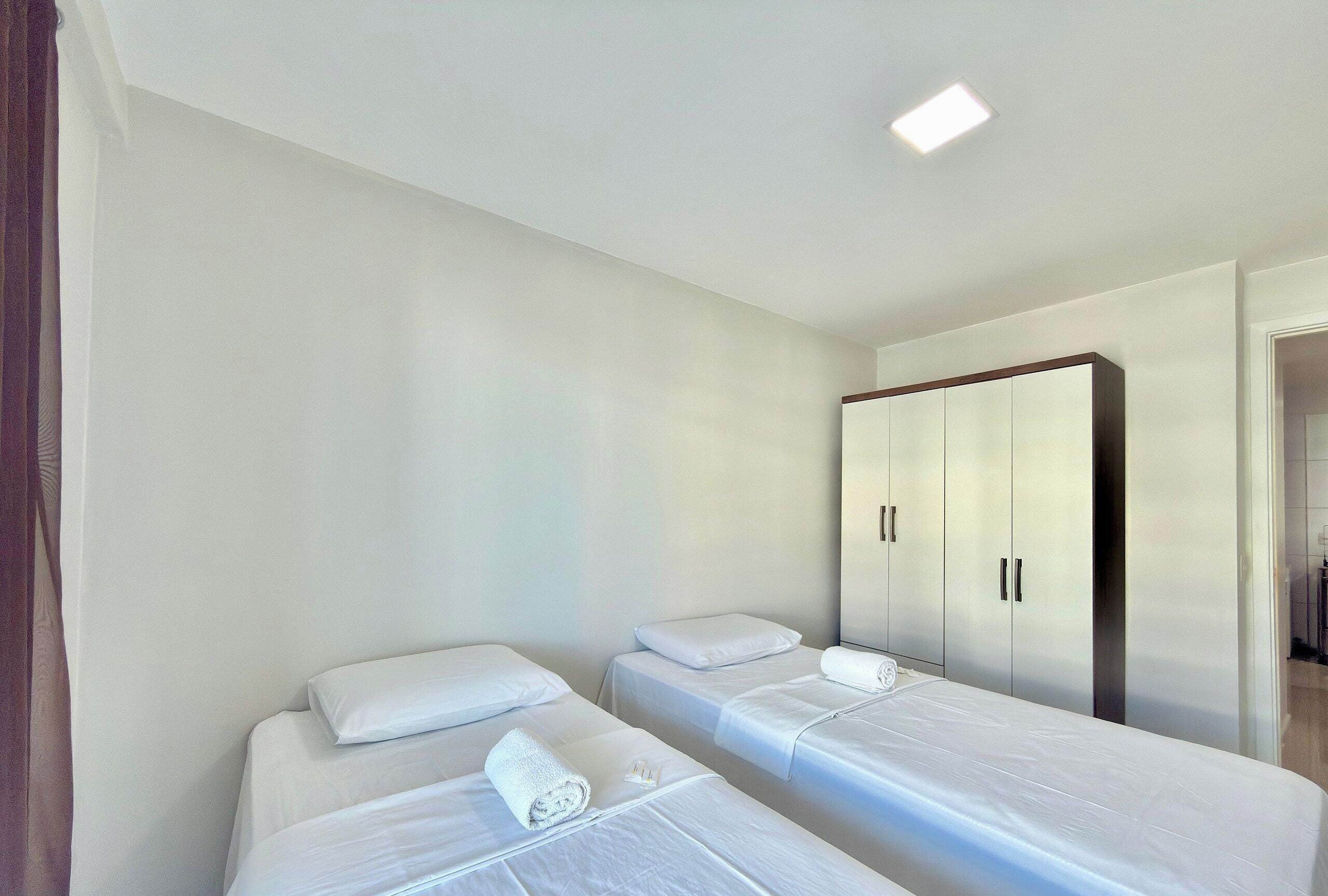 A hotel room with two single beds, a wardrobe, and a small bathroom.