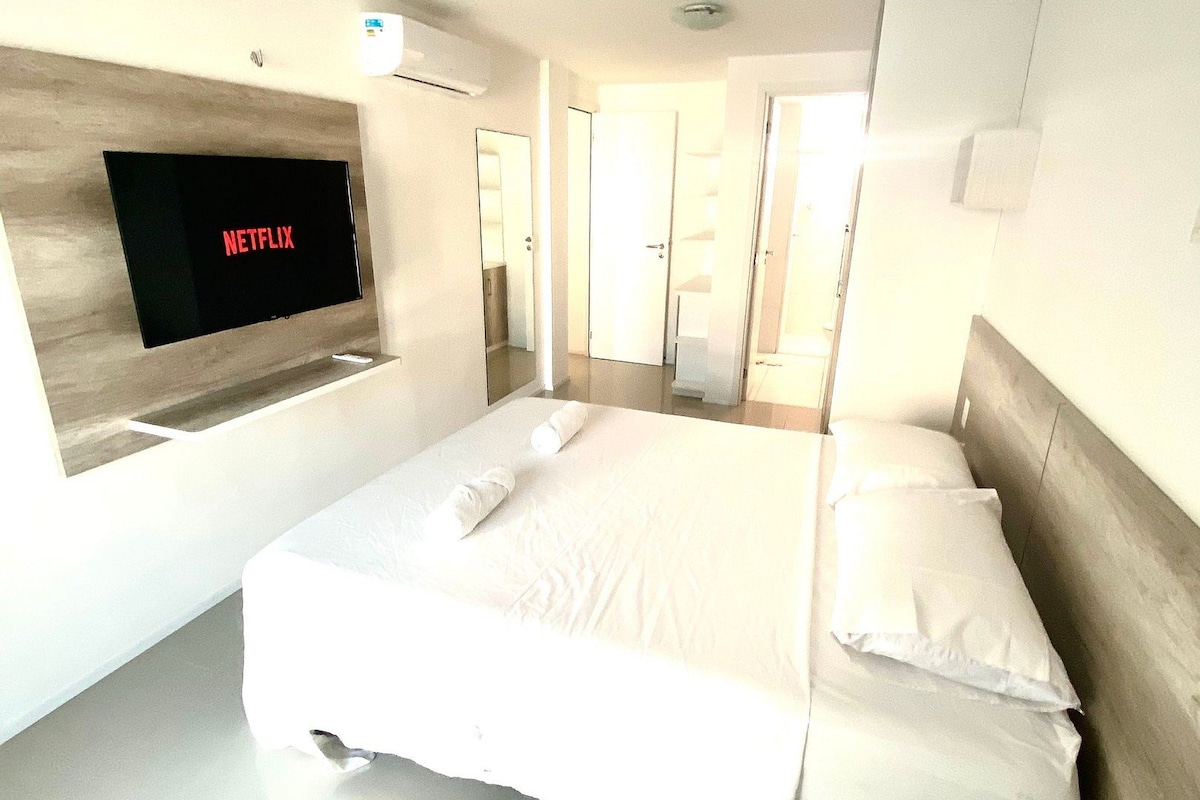 A modern hotel room with a large bed, a flat-screen TV mounted on the wall, and a minimalist design.