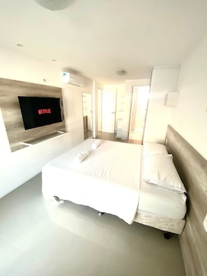 A modern hotel room with a large bed, a flat-screen TV mounted on the wall, and a minimalist design.
