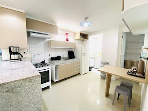 A modern kitchen with a stove, oven, coffee maker, and a dining area with stools.