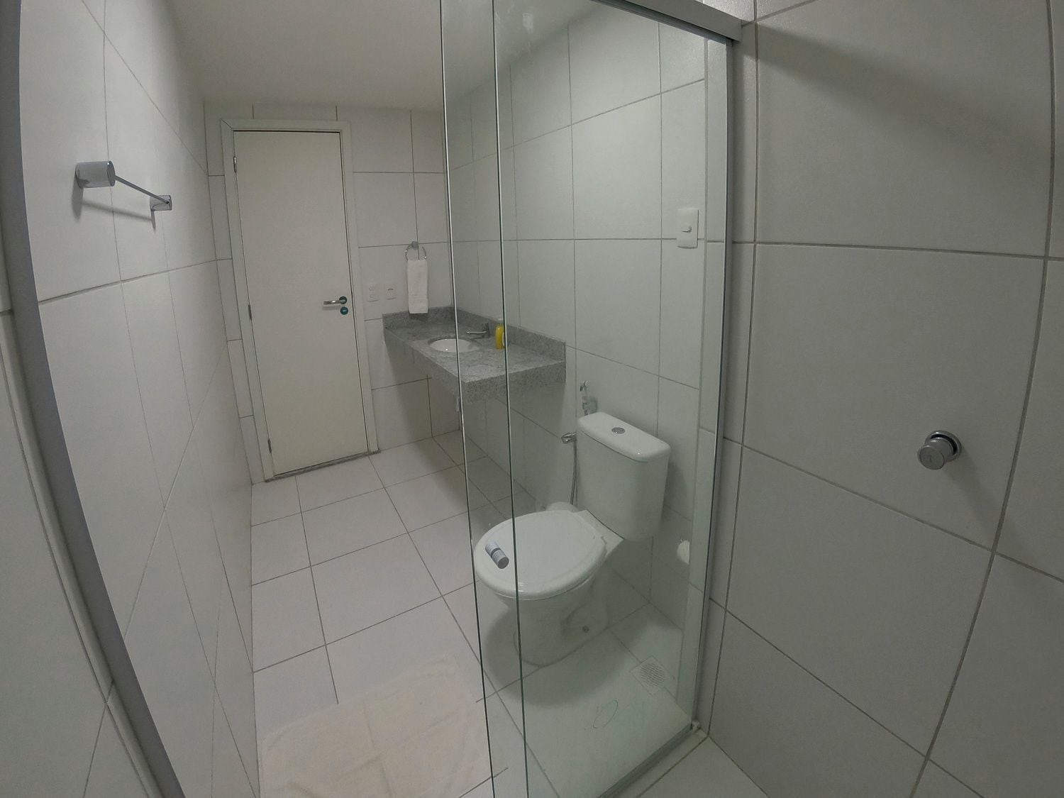 Et badeværelse med glasvæg omkring brusebad, toilet og vask.