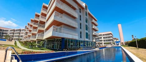 A modern hotel with a pool, multiple balconies, and a clear blue sky.