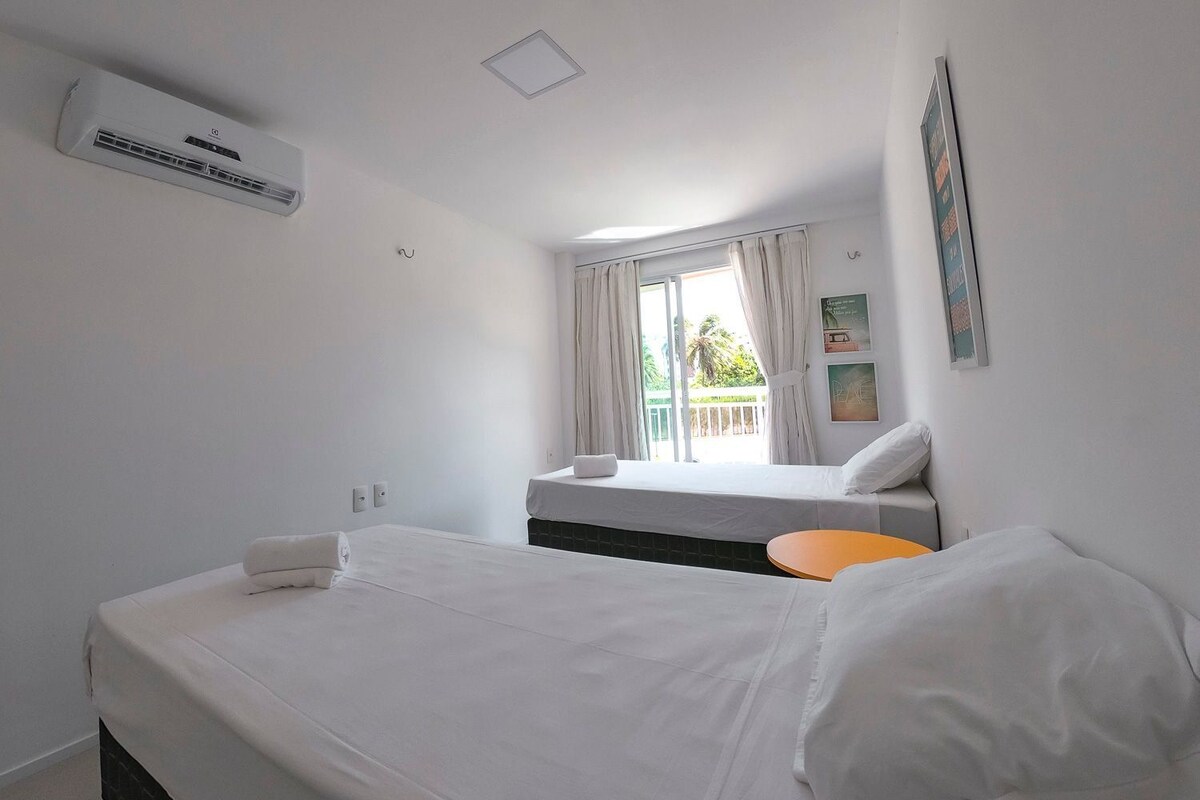 Una habitación de hotel con cama, una mesita, ventana con cortinas y equipo de aire acondicionado.