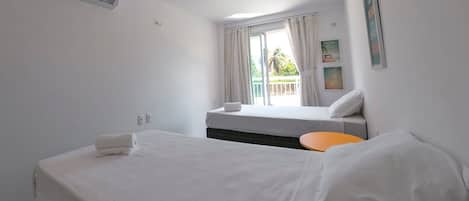 A hotel room with a bed, a small table, a window with curtains, and an air conditioning unit.