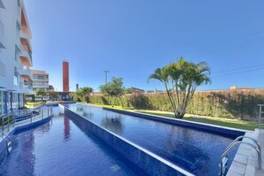 A swimming pool with a clear blue sky, a tall red chimney, and a building with balconies. - Solarium Residence Resort (Aquiraz)