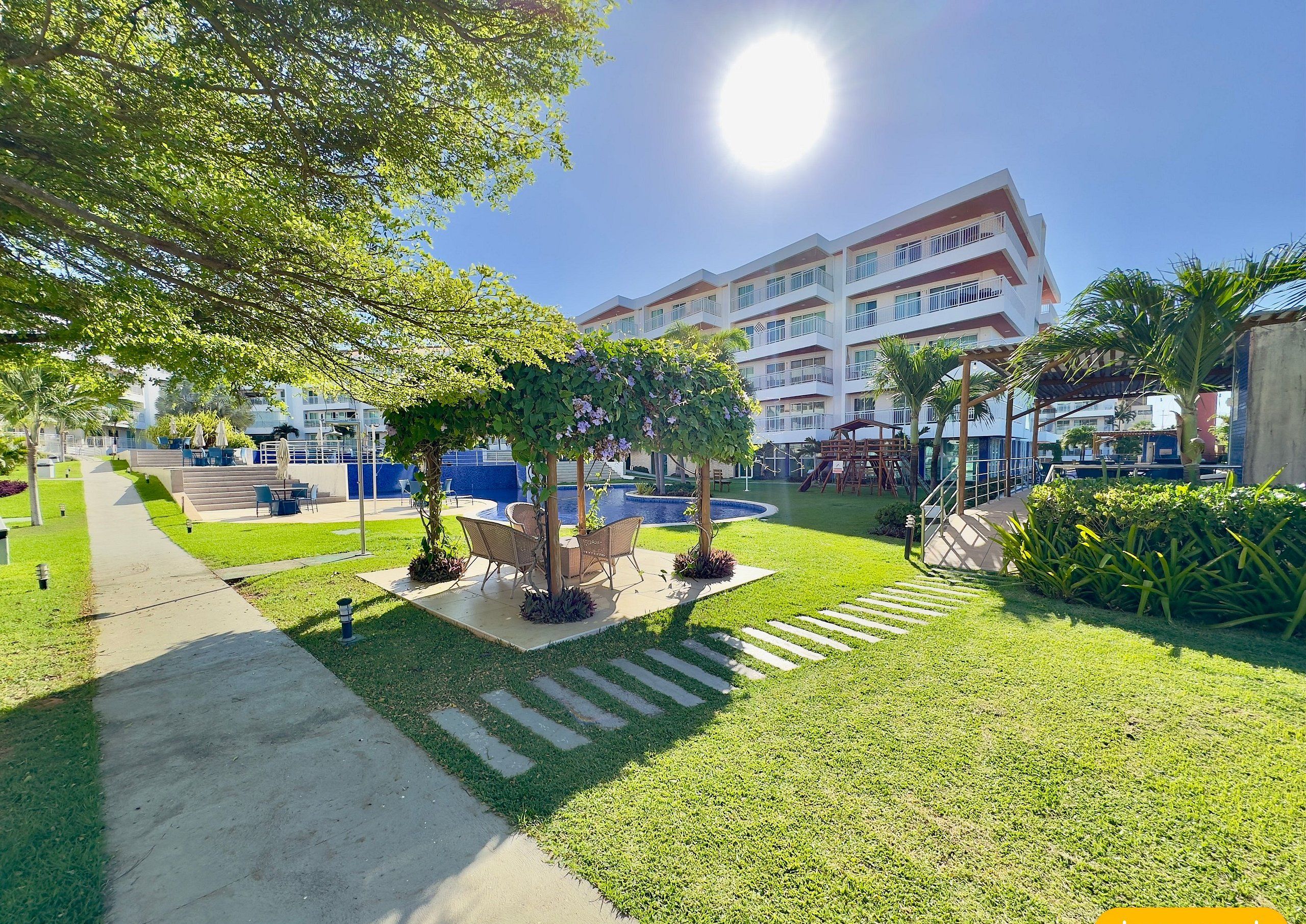 Un pati d'hotel amb una piscina, mobiliari exterior i un parc infantil.