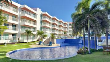 A hotel with multiple balconies, a swimming pool, and palm trees.
