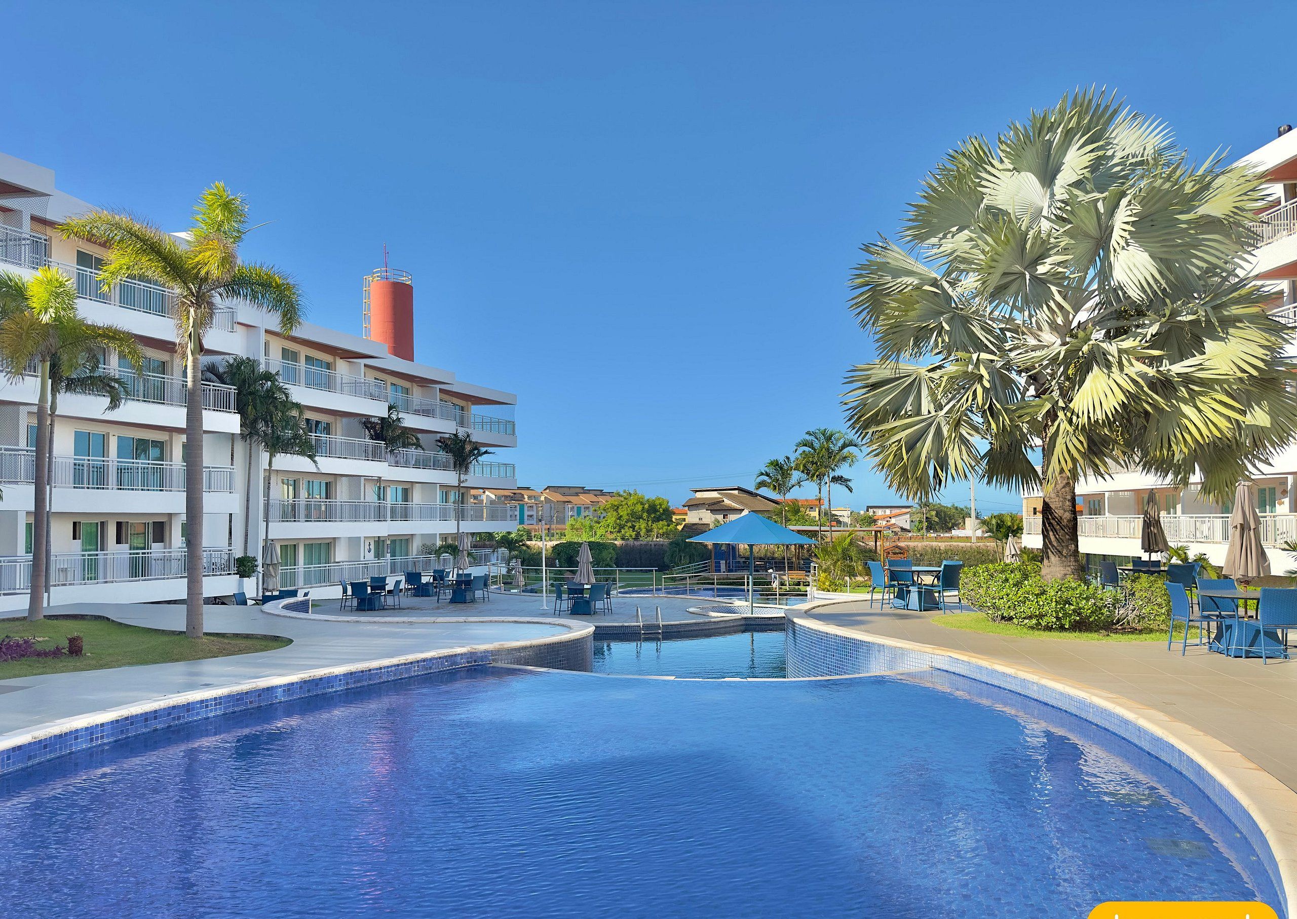 Hotel com piscina, palmeiras e áreas de estar ao ar livre.