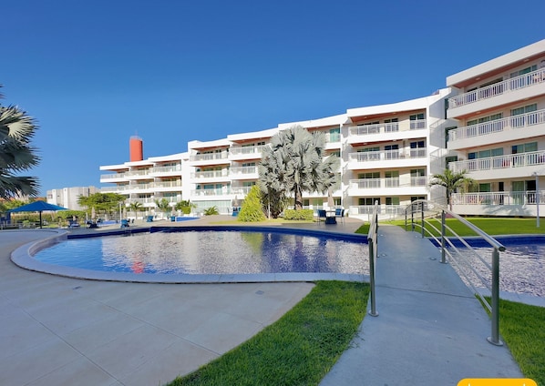 A hotel with a swimming pool, outdoor seating, and a well-maintained lawn.