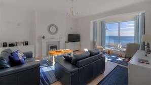 A modern living room with a fireplace, a television, and a view of the sea. - 2 Mareeba (Seaton)