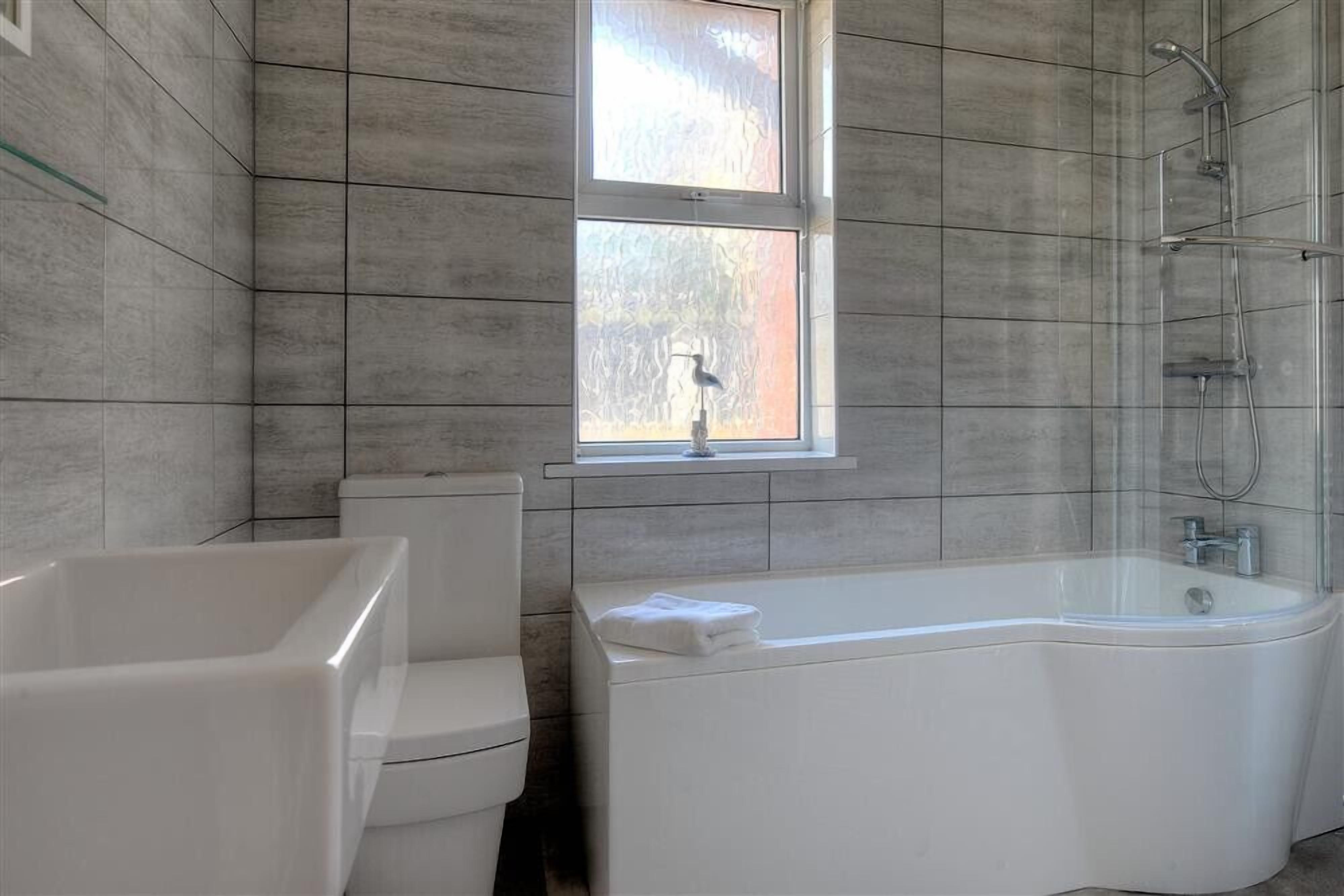 A bathroom with a bathtub, toilet, and a window.