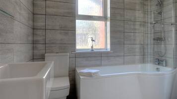 A bathroom with a bathtub, toilet, and a window.