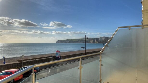 A coastal view from a balcony with a clear sky, a road with parked cars, and a distant cliff. - 2 Mareeba (Seaton)
