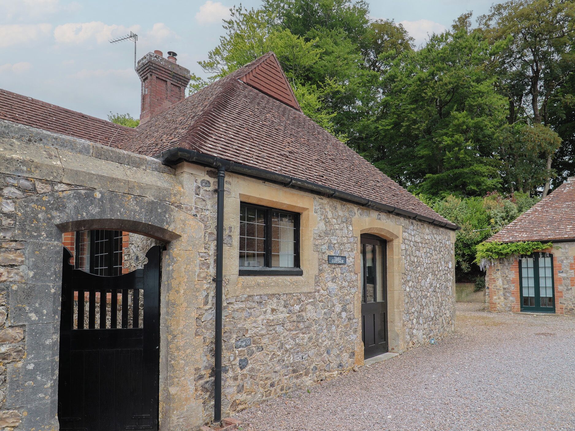 A stone cottage with a tiled roof, a black gate, and a sign reading "Yard Cottage."